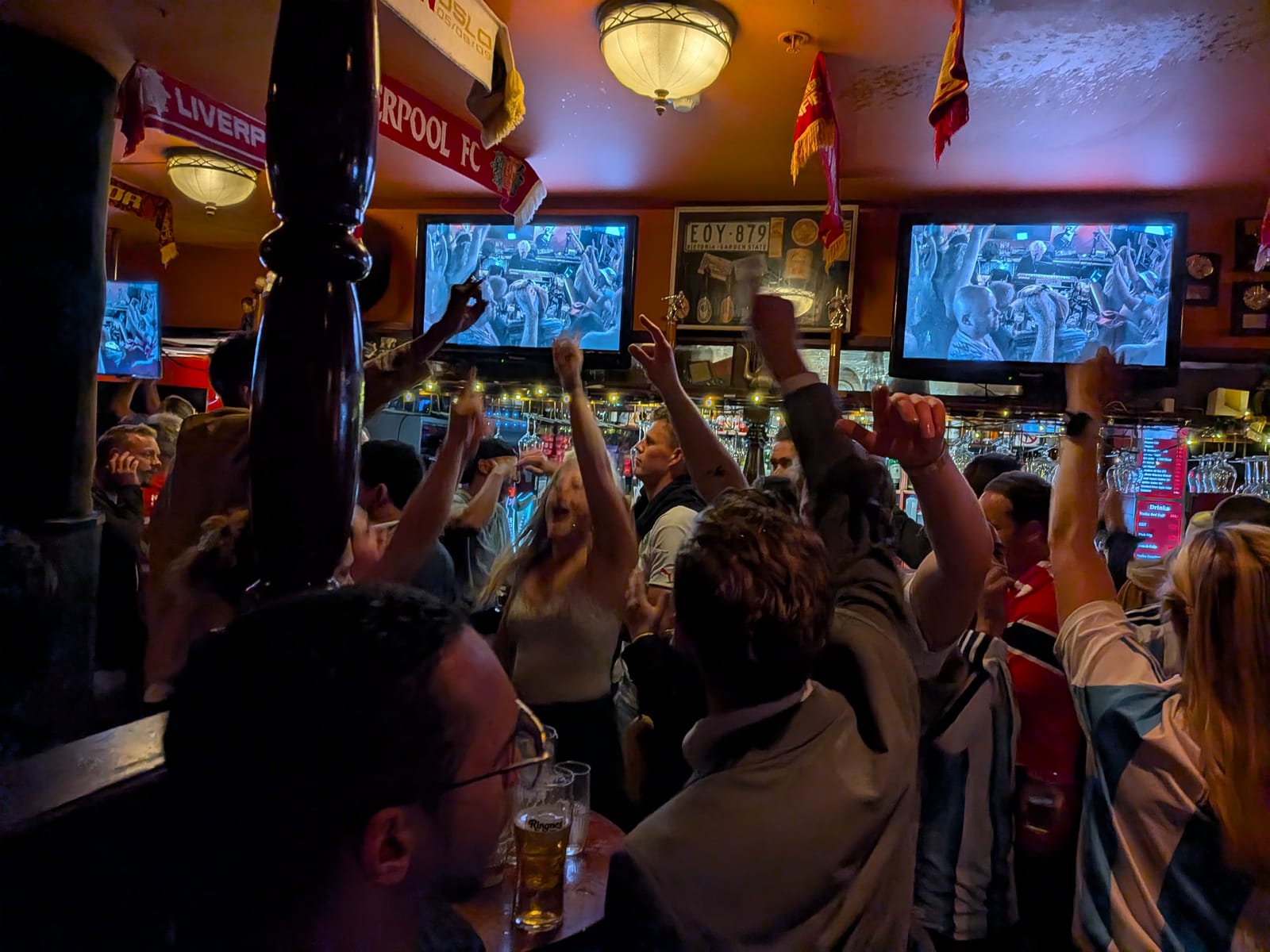 Celebrating inside the pub afterwards, arms up, a Liverpool scarf in the crowd